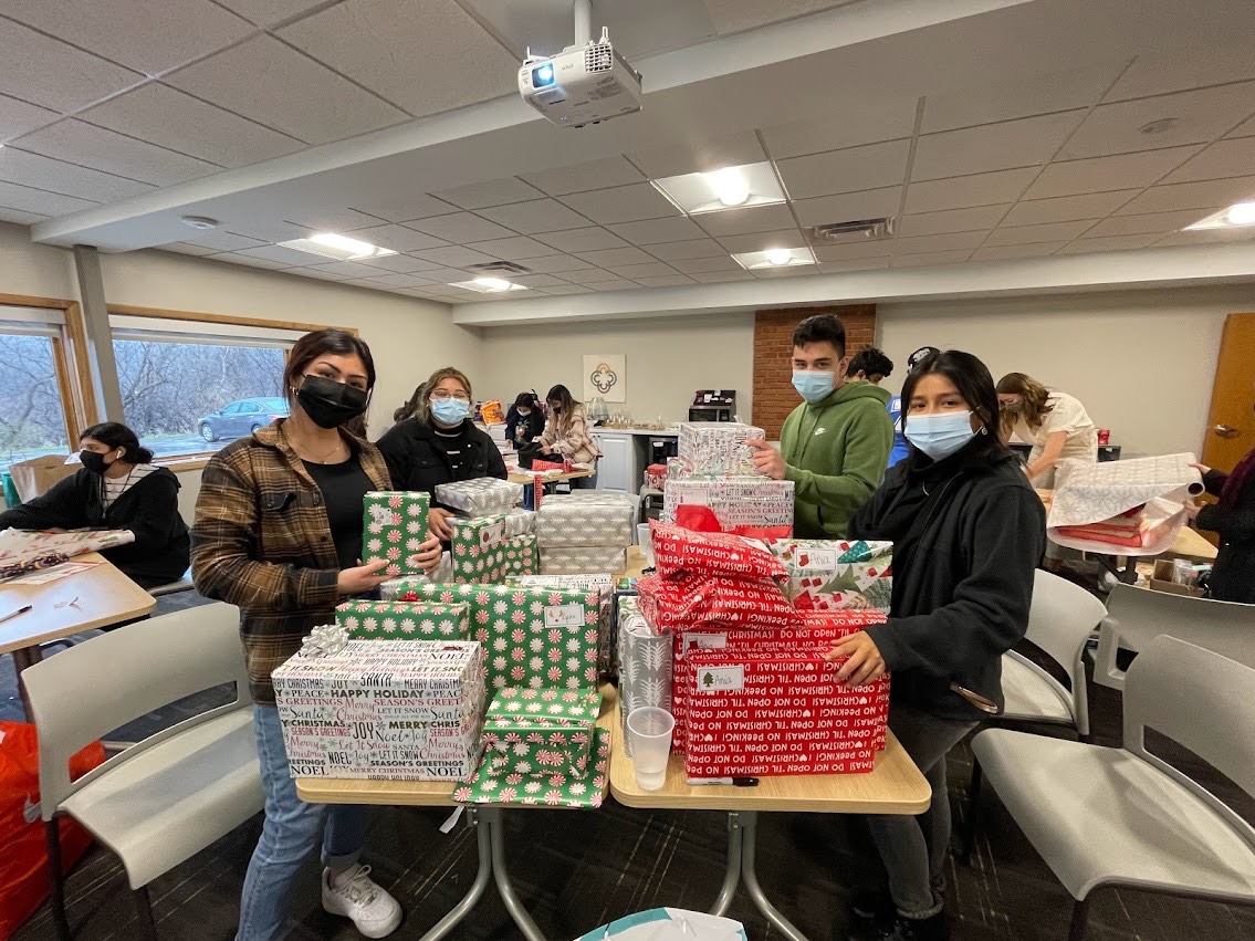 students smiling at camera in masks while wrapping holiday gifts